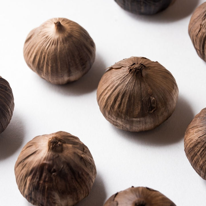 Fermented black garlic herb in a 0.25 kg pot from Sharbatly, showcasing dark, aged garlic cloves in a natural setting.